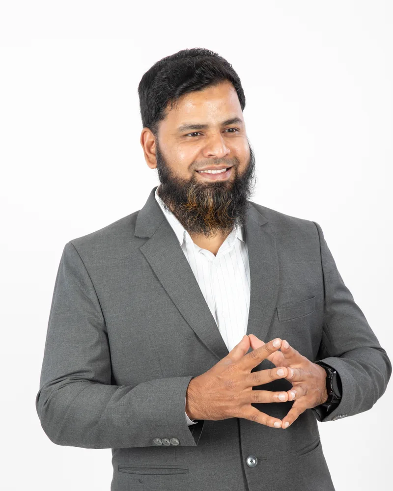 Abdul Lathif in a grey suit, smiling, hands steepled